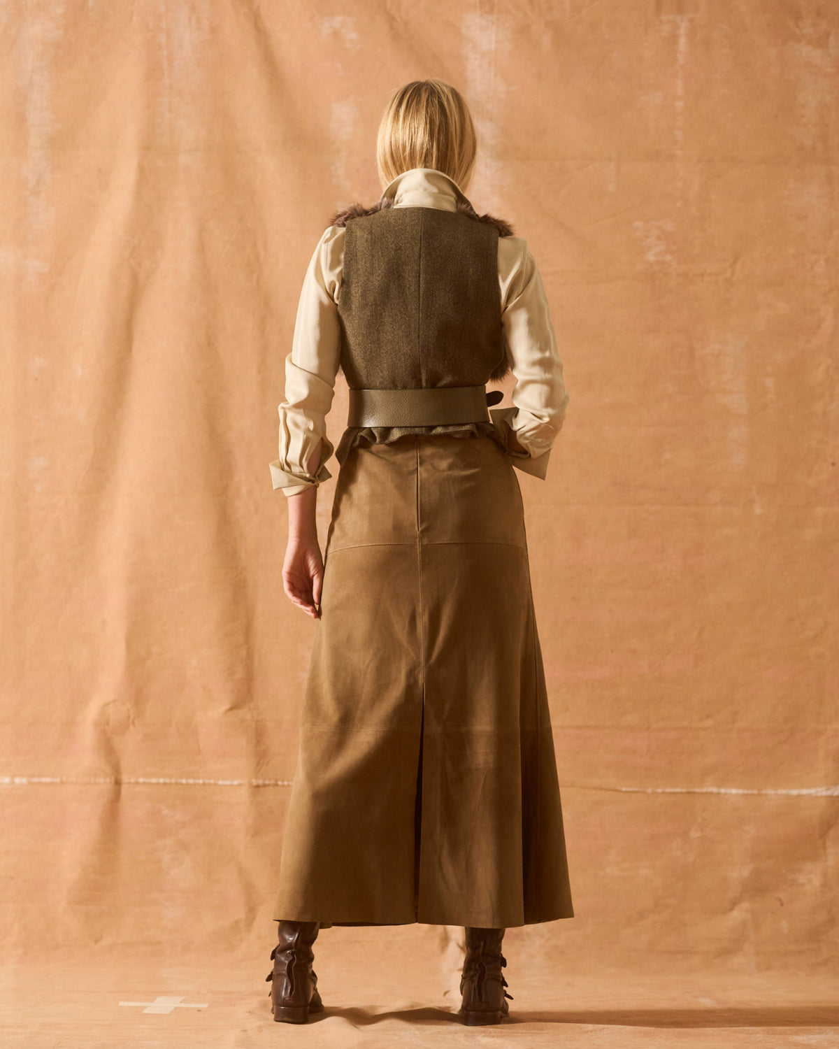 Three-quarter back view of model demonstrating the fit of the khaki leather Toscana Belt over a vest and skirt for women by T.ba