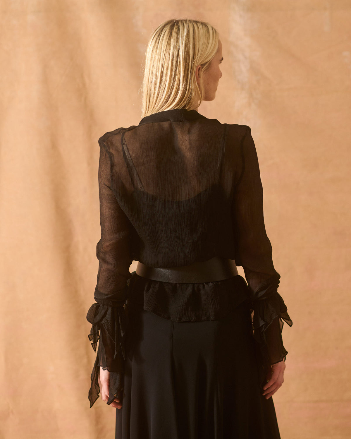 Medium back view of model wearing the wide black leather Toscana Belt styled over a sheer black blouse for women by T.ba