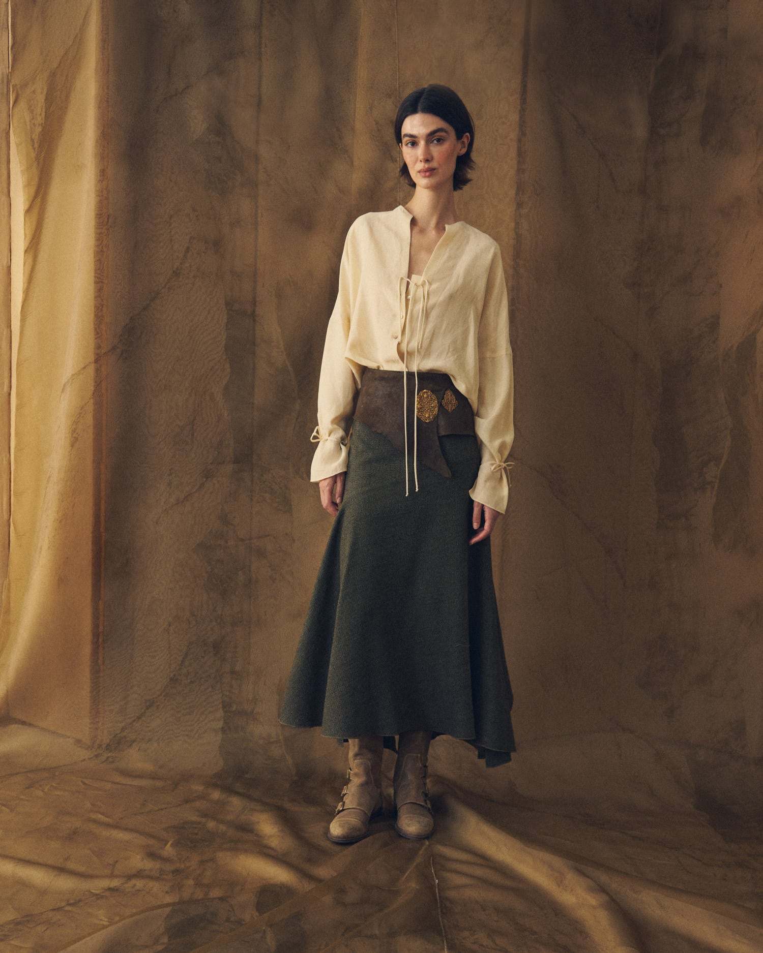 Full-length front view of model wearing the Toscana long tweed skirt in dark green styled with a leather sash belt by T.ba