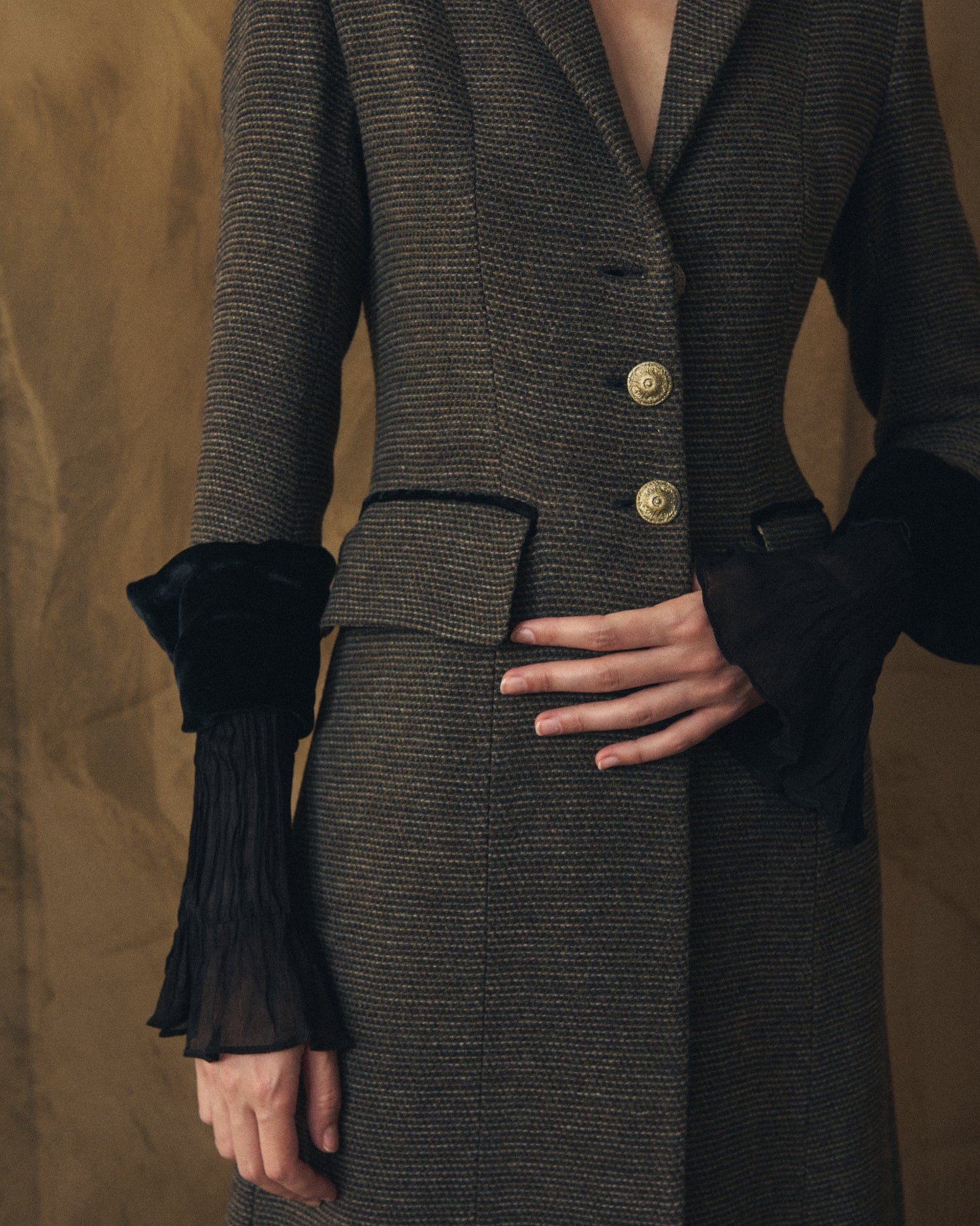 Close-up of women's Tweed Classic Combi coat showing grey wool texture, carved gold buttons, and pleated cuffs by T.ba