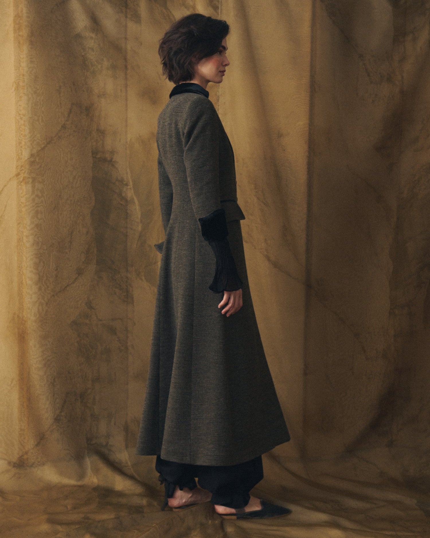 Side profile view of women's Tweed Classic Combi long coat in grey wool with velvet cuff details by T.ba