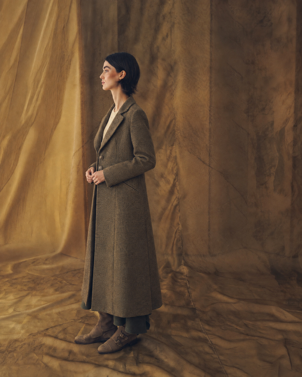 Full length front view of model wearing the long Tweed Lancelot Combi Coat in brown wool tweed with tailored lapels for women by T.ba