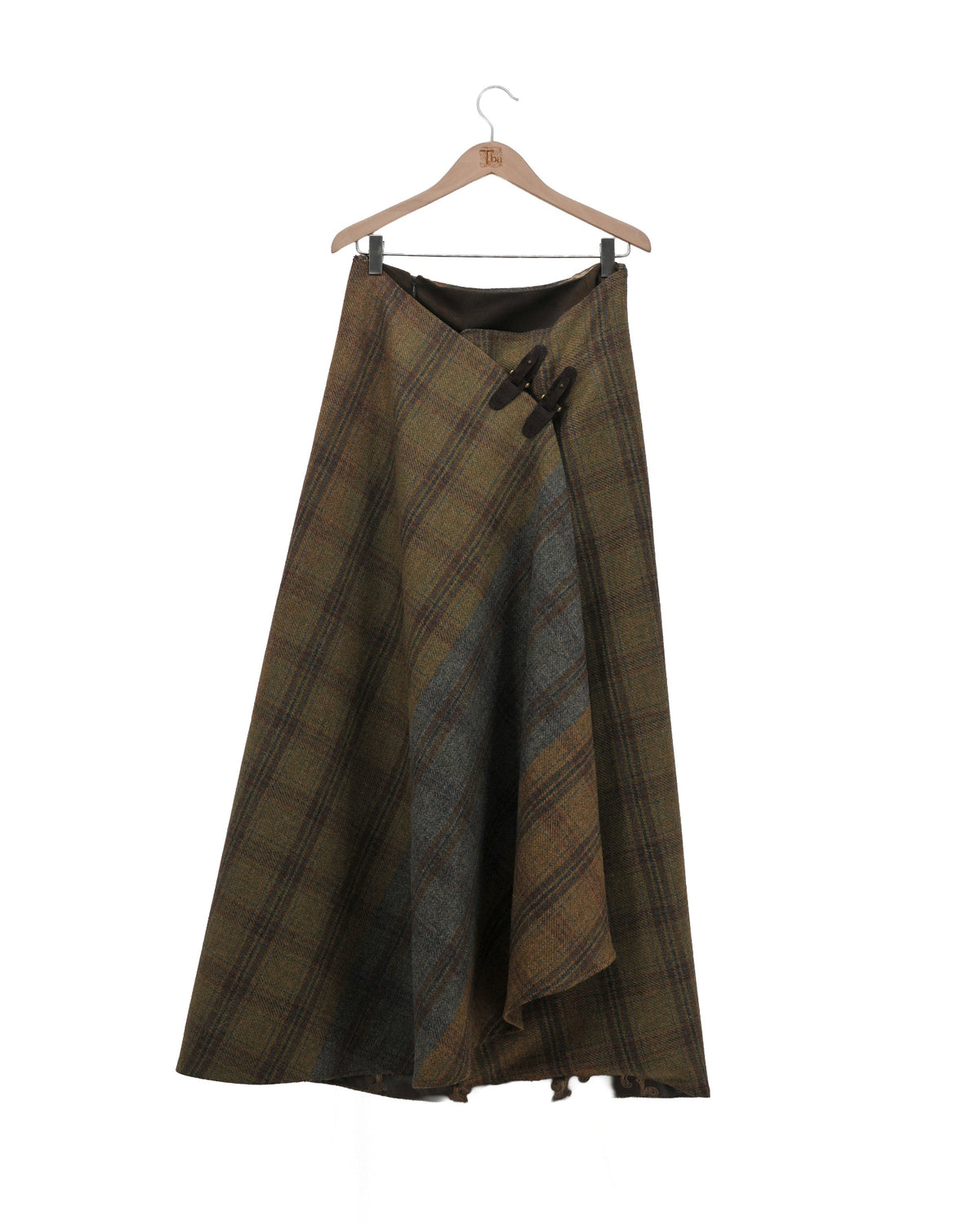 Product shot on hanger showing the front view of the wrap-style Tweed Lancelot Skirt Mix with asymmetric drape and leather buckle detail in plaid wool for women by T.ba