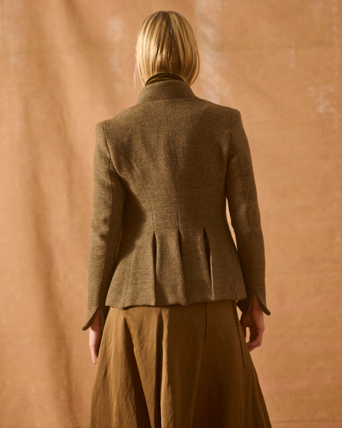 Back view of model wearing the Tweed Sam Jacket in brown wool tweed highlighting the structured pleated back hem detail for women by T.ba