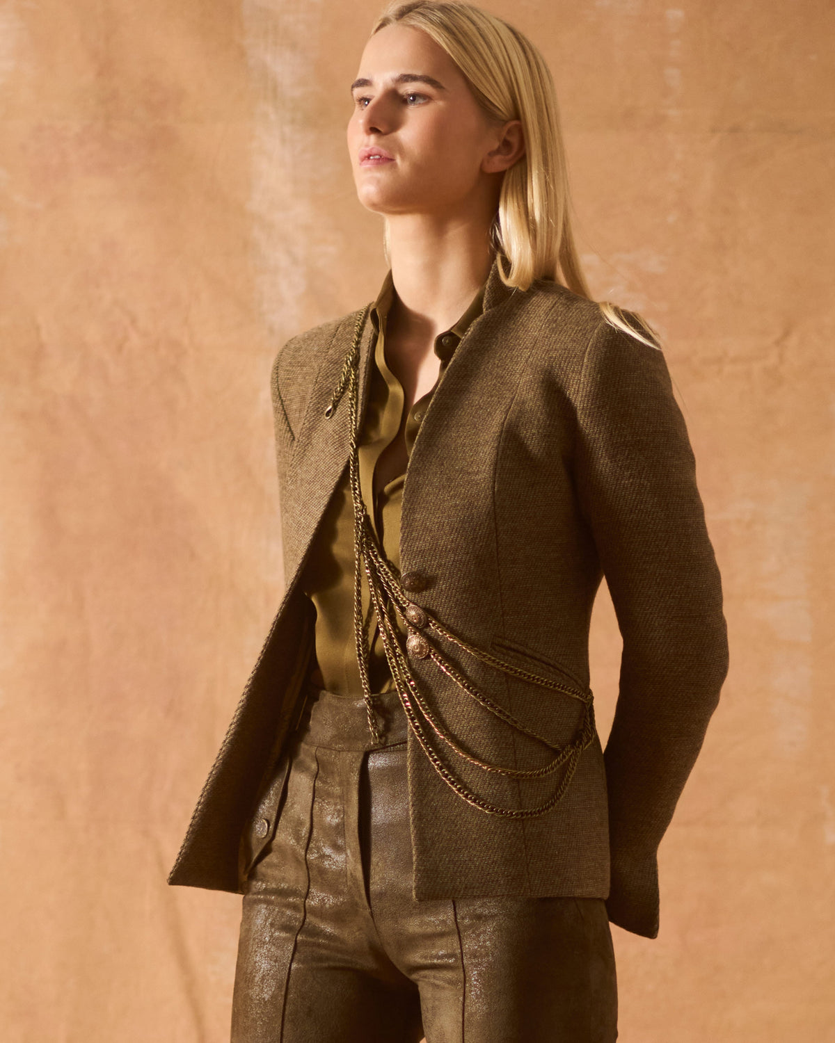 Three-quarter view of model showing the structured Tweed Sam Jacket in brown wool tweed with draped gold-tone chains for women by T.ba