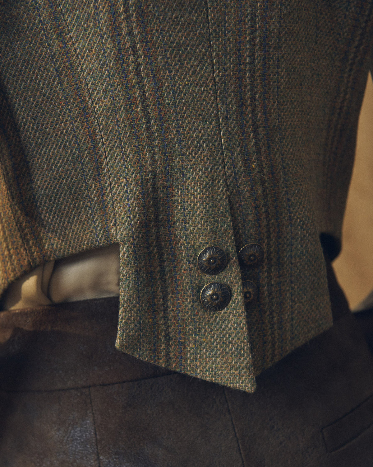 Close-up shot of the Tweed Short Baltea Vest back hem highlighting the green herringbone tweed texture and antique buttons by T.ba.