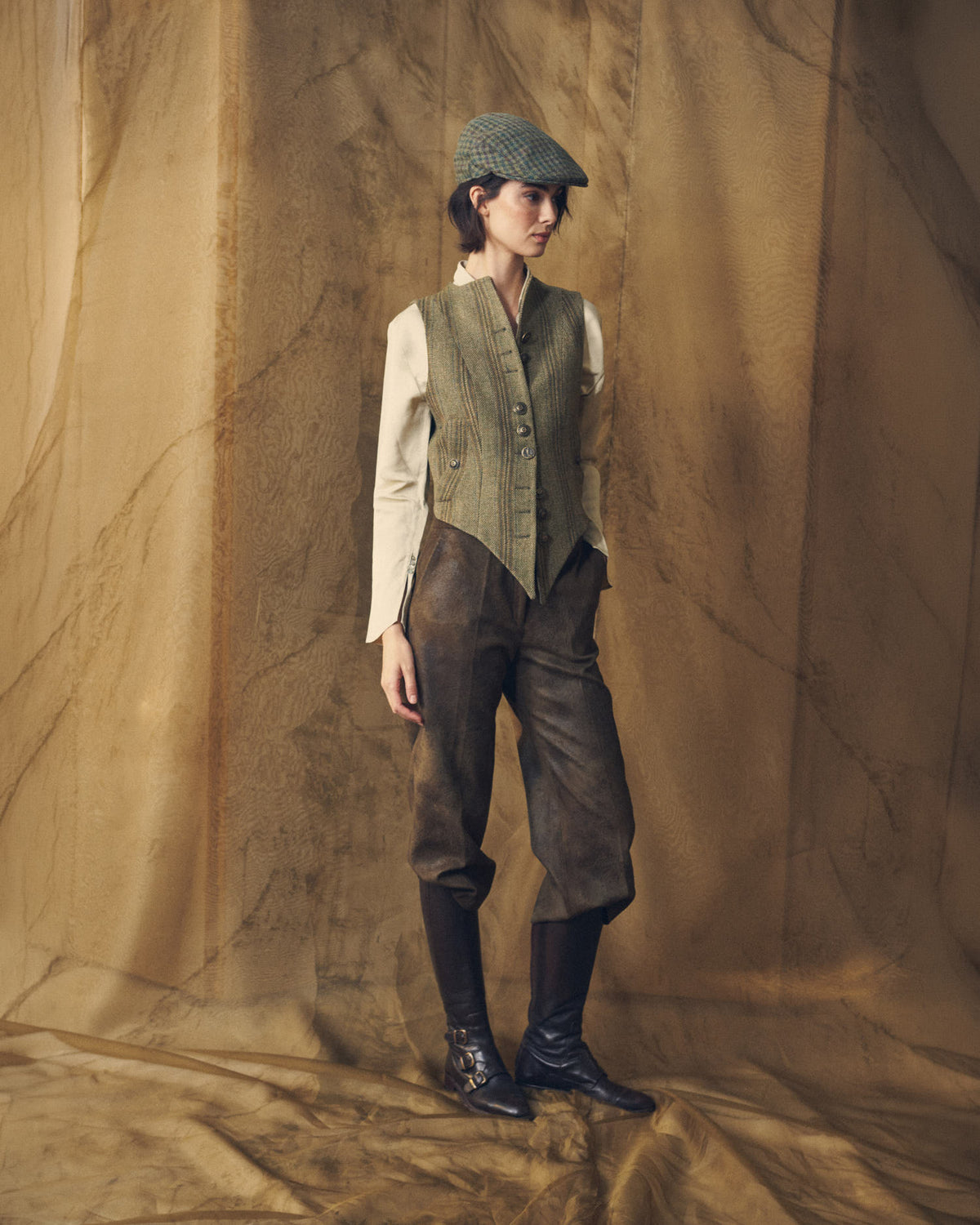 Full-length side-angle view of a model styled in the Tweed Short Baltea Vest with brown leather trousers for women by T.ba.