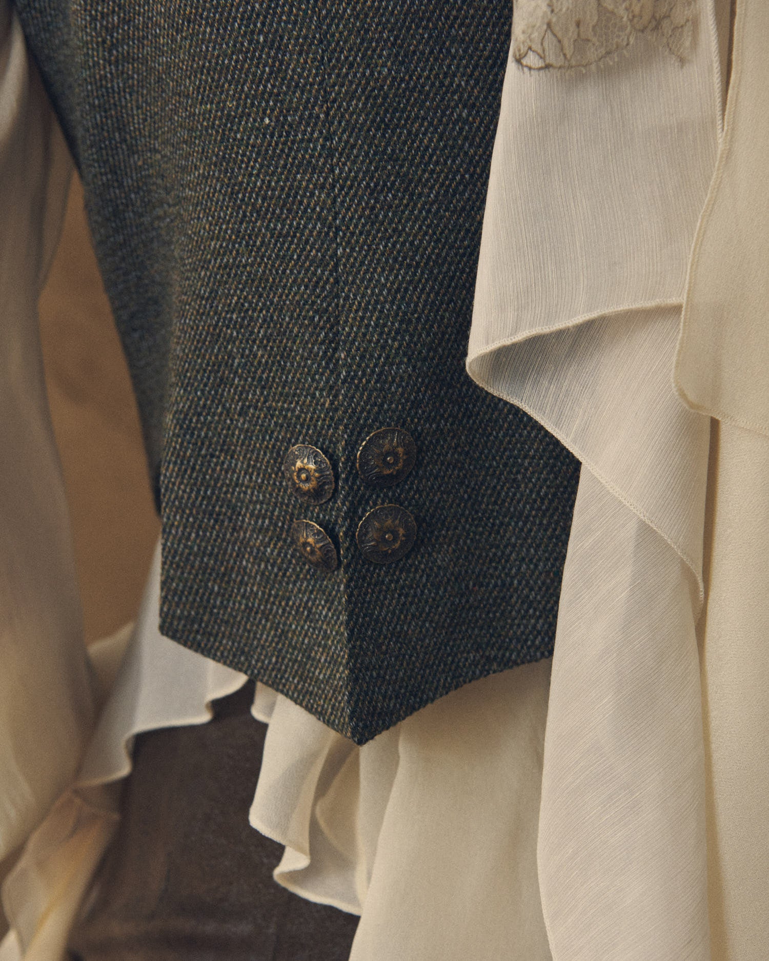 Close-up shot of the Tweed Short Baltea Vest showing the back hem and four ornate brass buttons by T.ba.