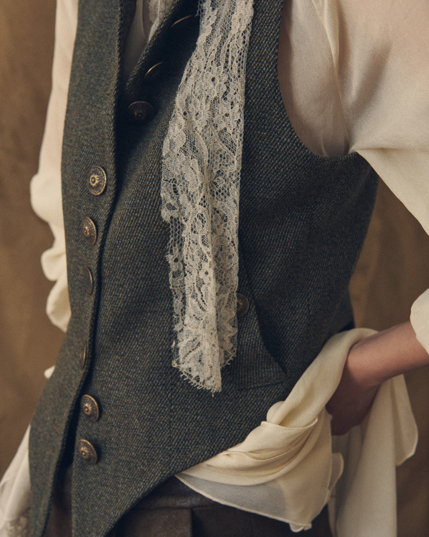 Close-up shot of the Tweed Short Baltea Vest in slate green herringbone wool highlighting the texture and button closure by T.ba.