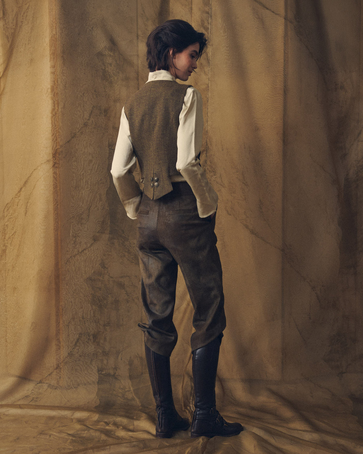 Three-quarter rear view of model showcasing the back tailored structure and hem of the Tweed Short Baltea Vest in brown wool for women by T.ba