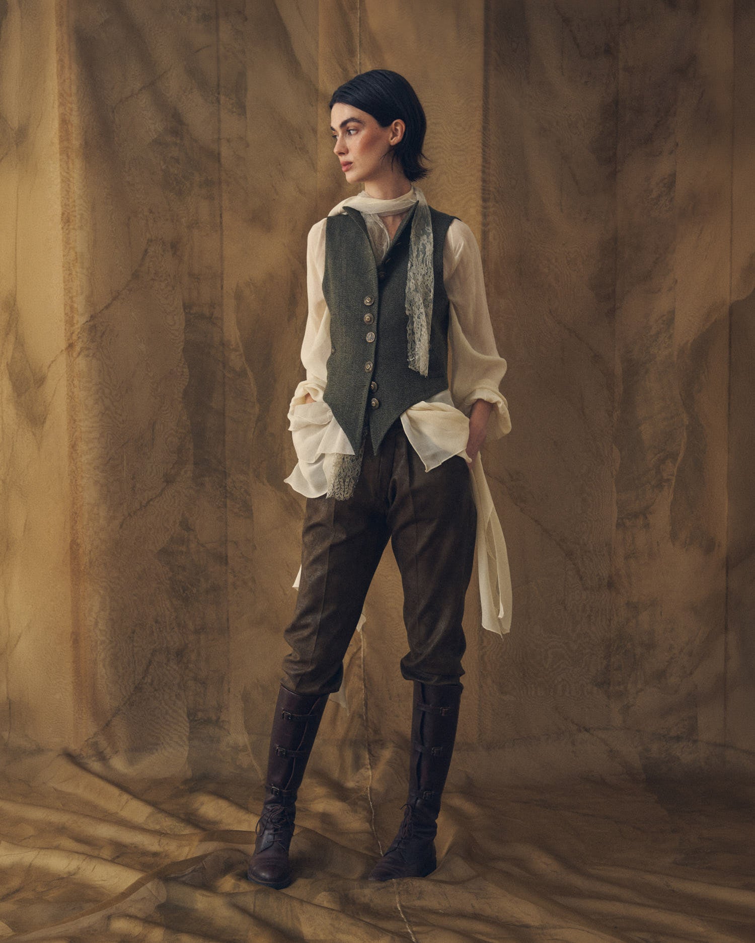 Full-length view of the Tweed Short Baltea Vest in slate green wool with a pointed front hem and brass buttons by T.ba.