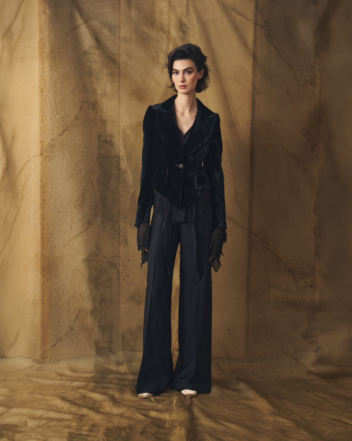 Full-length view of model wearing the black Verdi silk velvet jacket with asymmetrical hem paired with wide-leg trousers by T.ba