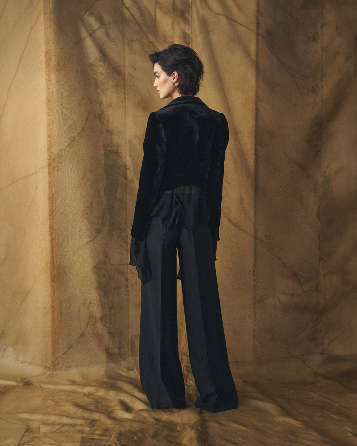Three-quarter back view of model wearing the tailored black Verdi short silk velvet jacket by T.ba